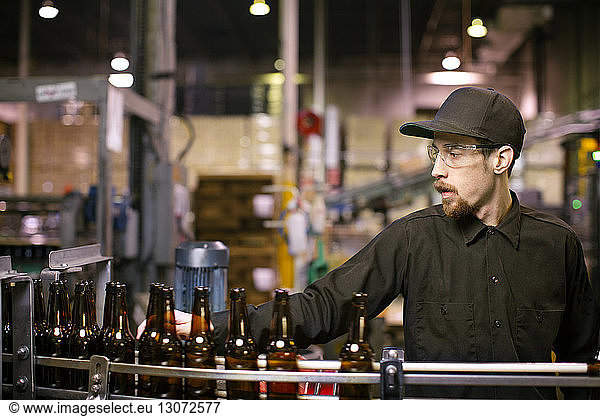 Man looking at beer bottles on conveyor belt in brewery