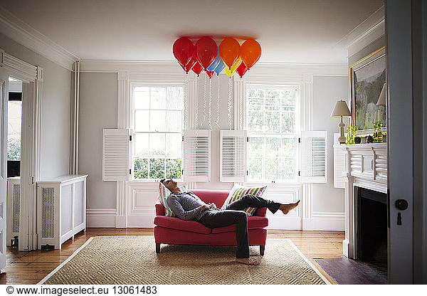 Man looking at helium balloons while lying on sofa