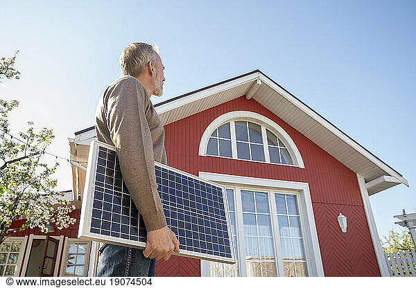Man looking at house holding solar panel