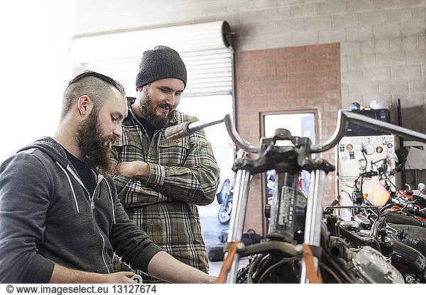 Man looking at mechanic working on motorcycle at auto repair shop