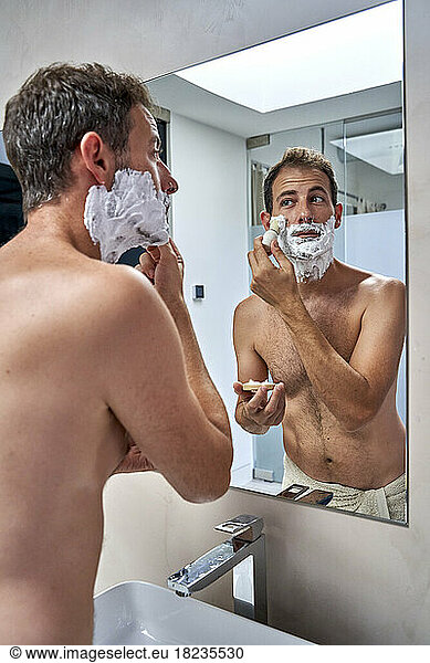Man looking at mirror reflection and shaving in bathroom
