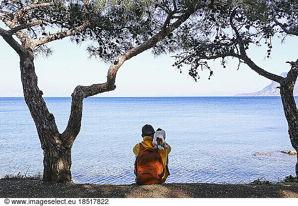 Man looking at sea sitting with dog under tress