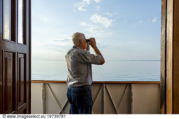 Man looking at sea through binoculars from ship