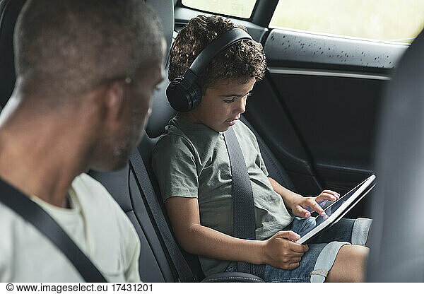 Man looking at son watching video on digital tablet in electric car