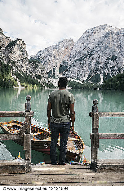 Man looking at view while standing by wooden railing by lake against mountains