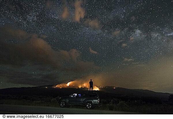 Man looking at wildfire while standing on off-road vehicle against star field