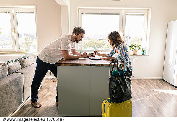Man looking at woman filling form while standing with luggage in apartment during staycation