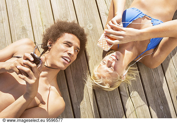 Man looking at woman using smartphone while lying on boardwalk