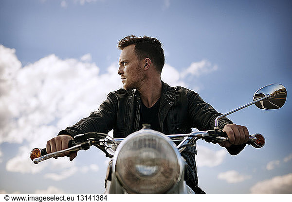 Man looking away while riding motorcycle against sky