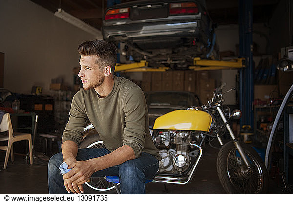 Man looking away while sitting on stool in garage
