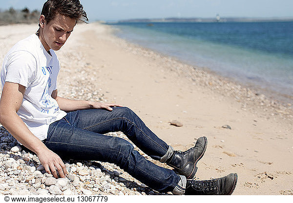 Man looking down while sitting on shore at beach