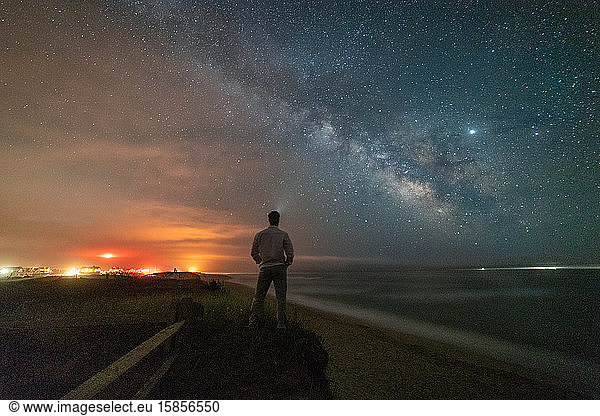 Man looking out at Milky Way galaxy over the beach in Nantucket.