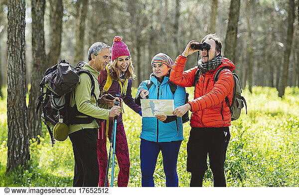 Man looking through binoculars standing by friends sharing map in forest