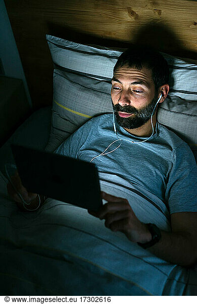 Man lying on bed with tablet in darkness