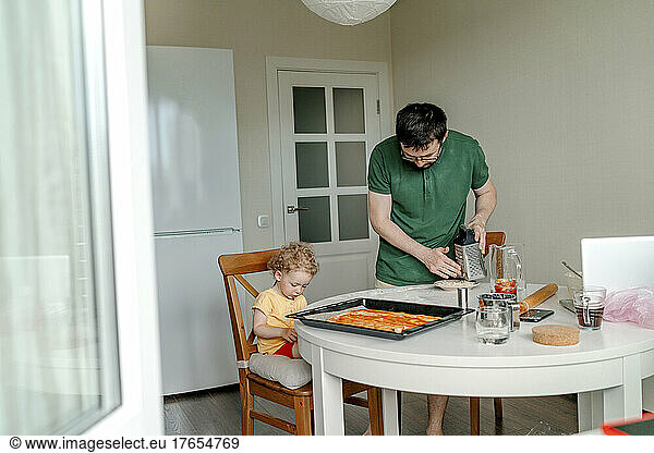 Man making pizza by daughter sitting on chair in kitchen