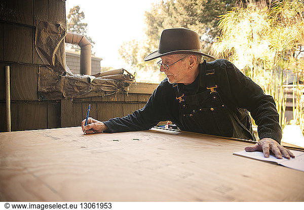 Man marking on wooden plank with pen at workshop