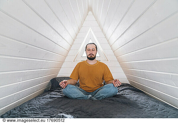 Man meditating sitting on bed in attic of country home