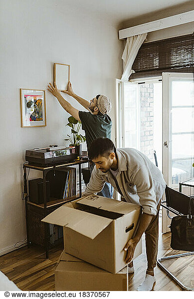 Man mounting frame on wall with boyfriend stacking cardboard boxes at home