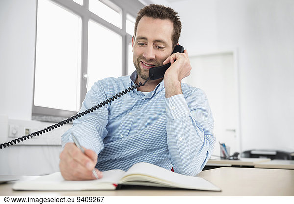 Man office landline telephone writing memo