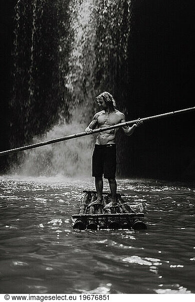 Man on a bamboo raft on a mountain river near a waterfall  Bali.