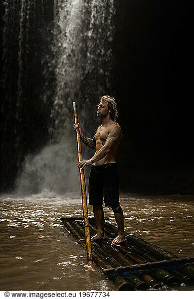 Man on a bamboo raft on a mountain river near a waterfall  Bali.