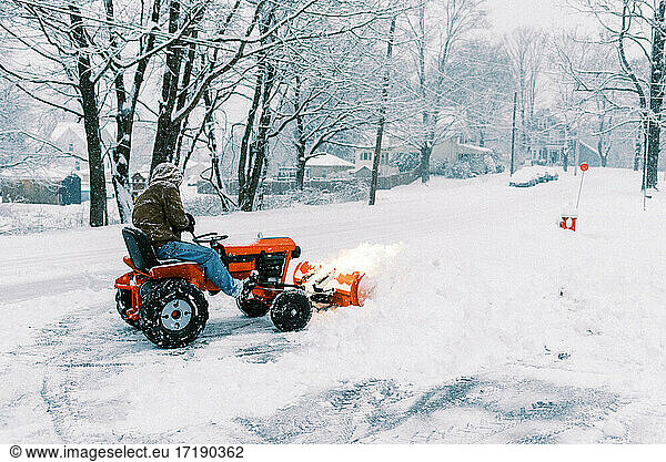 Man on a tractor plowing snow in a driveway during a nor'easter storm