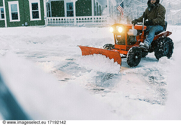 Man on a tractor plowing snow in a driveway during a nor'easter storm