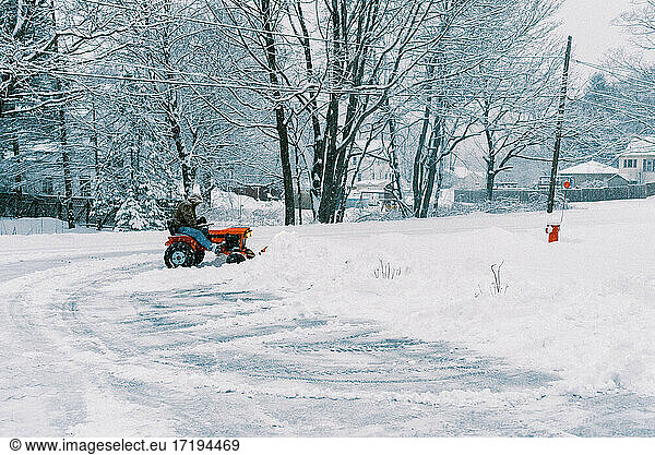 Man on a tractor plowing snow in a driveway during a nor'easter storm