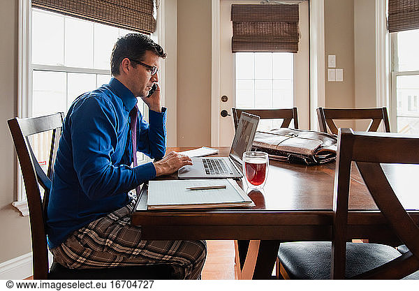 Man on cellphone working from home using a computer in pyjama pants.