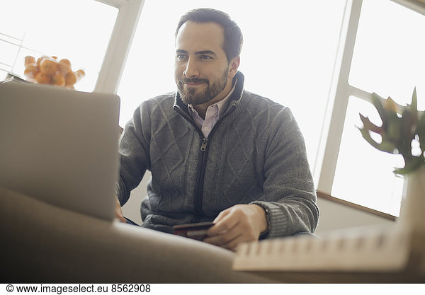 Man on-line shopping on laptop on sofa with credit card