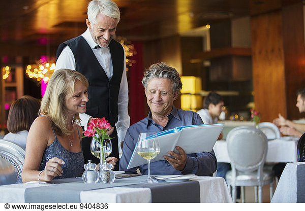 Man ordering meal at fancy restaurant table  waiter standing behind