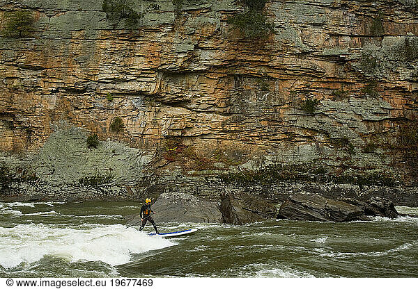 Man paddleboarding on a river.