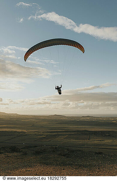 Man paragliding under cloudy sky at sunset