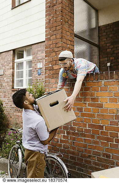 Man passing cardboard box to boyfriend while leaning on brick wall
