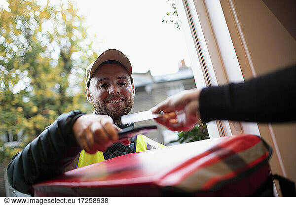 Man paying delivery man for food delivery with smart card at front door