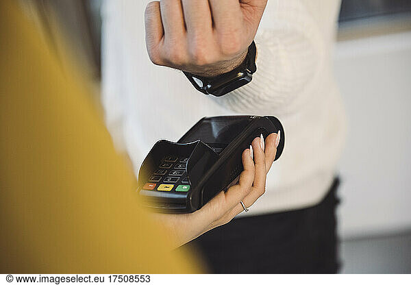 Man paying through smart watch to waitress holding credit card reader in cafe