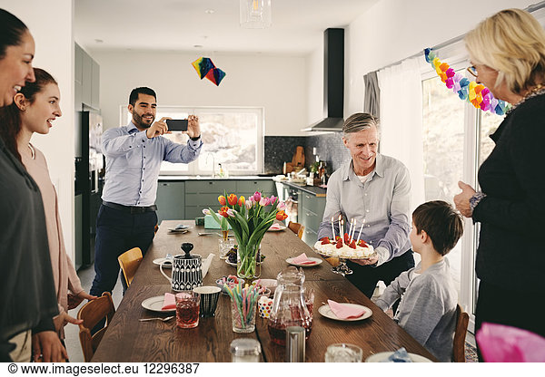 Man photographing boy with family during birthday party through smart phone