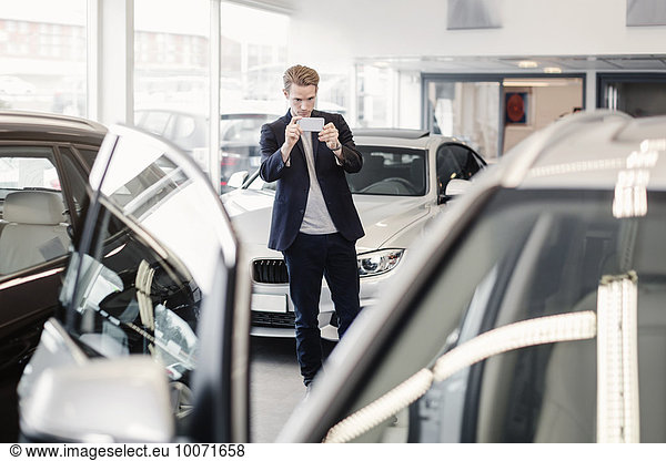 Man photographing car through smart phone at dealership store