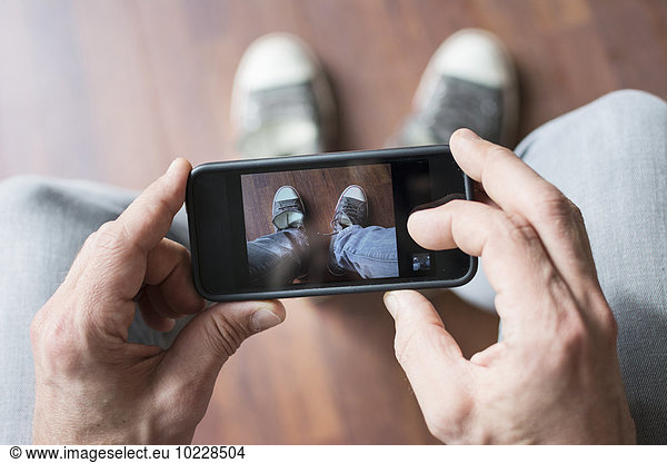Man photographing his shoes with smartphone