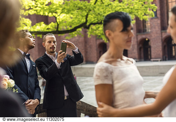 Man photographing lesbian couple during wedding ceremony
