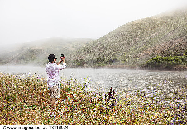 Man photographing mountains with smart phone in foggy weather