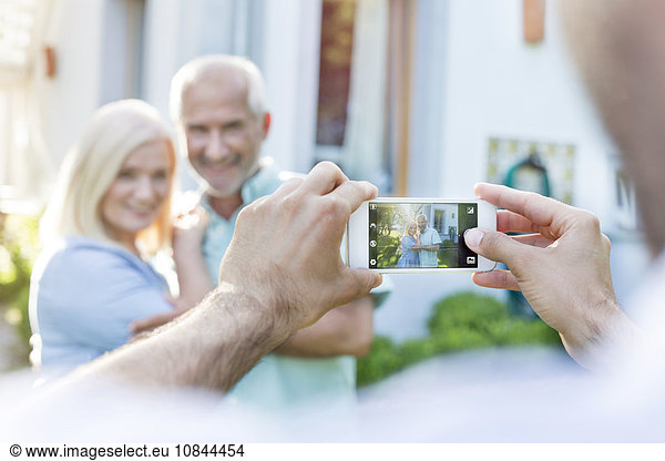 Man photographing senior couple with camera phone