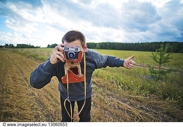Man photographing while standing on grassy field against sky