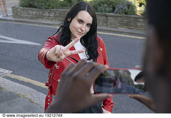 Man photographing woman showing peace sign gesture at street
