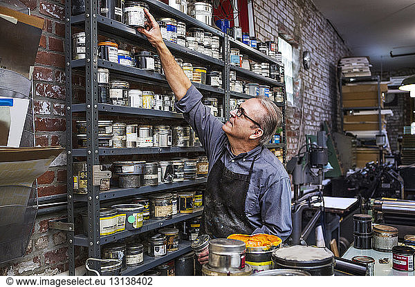 Man picking up ink container from shelves at letterpress workshop