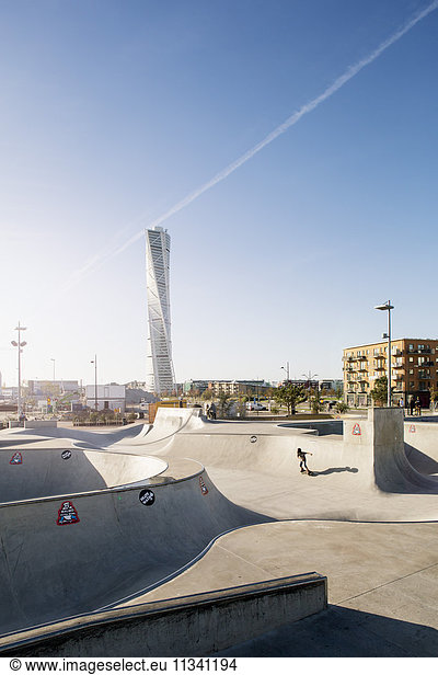 Man playing at skateboard park against Turning Torso in city on sunny day