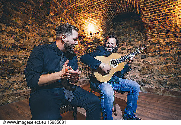 Man playing flamenco on guitar while singer clapping in nightclub