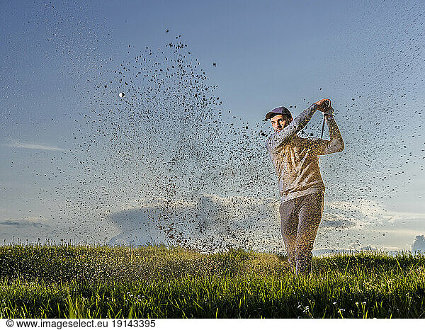 Man playing golf standing on grass at dusk
