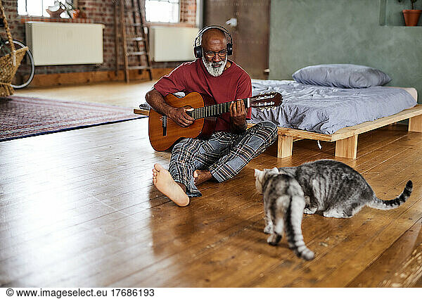 Man playing guitar in front of cats at home