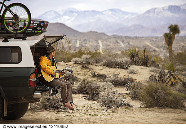 Man playing guitar while sitting on car trunk